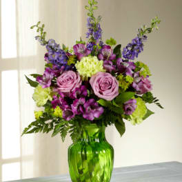 Purple and pink flower arrangement in a green glass vase