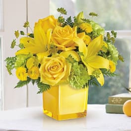 Yellow roses and lilies arranged in a square glass vase