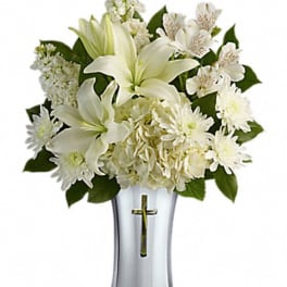 White lilies and daisies arranged in a silver vase with a cross