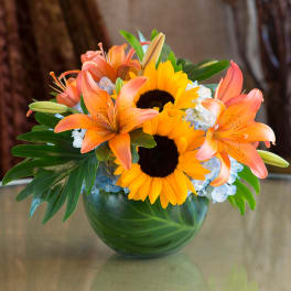 Bouquet of orange lilies and sunflowers in a green glass vase