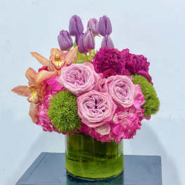 Pink and purple floral arrangement in a green glass vase