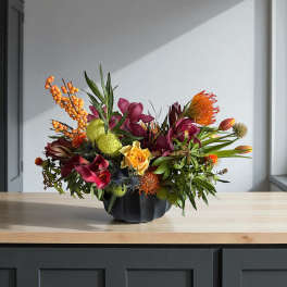 Colorful floral arrangement in a black vase with orange berries and burgundy blooms