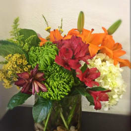 Mixed bouquet in a glass vase with orange lilies, red alstroemeria, and green chrysanthemums