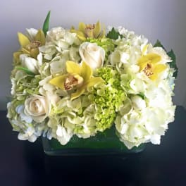 White hydrangea and roses with yellow orchids in a glass vase