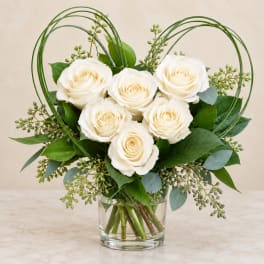White roses arranged in a glass vase with looping green wire accents