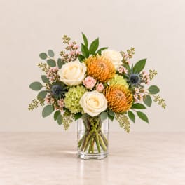 Bouquet of cream roses, orange pincushion blooms, and pink flowers in a glass vase