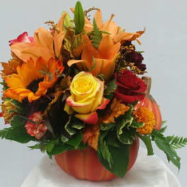 Autumn bouquet in a pumpkin-shaped vase with sunflowers, roses, and lilies
