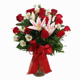 Bouquet of red roses and pink lilies in a glass vase with a red ribbon