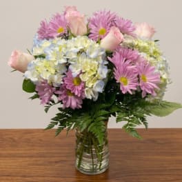 Pink daisies and roses arranged with pale hydrangeas in a glass vase