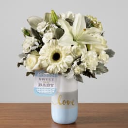 White floral bouquet in a blue and white vase with a baby tag