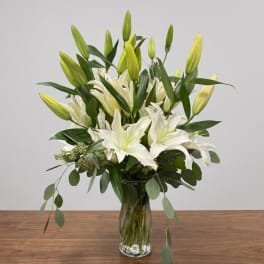 White lilies and unopened lily buds in a clear glass vase