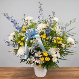 Mixed bouquet in a white vase with blue ribbon and yellow, white, and blue flowers