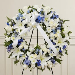 White and blue floral wreath with a white ribbon bow on a stand