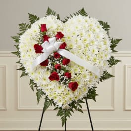 Heart-shaped white chrysanthemum wreath with red roses and a white ribbon on an easel