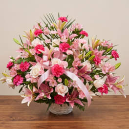 Pink and white floral arrangement in a wicker basket with a pink ribbon