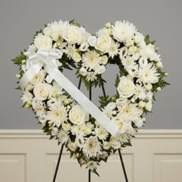 Heart-shaped white floral wreath on an easel with a white ribbon bow