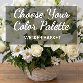 White floral arrangement in a wicker basket with lilies, roses, and daisies