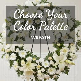 White floral wreath on a stand with lilies and daisies
