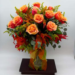 Orange roses arranged in a glass vase with autumn leaves and ribbon