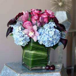 Pink roses and blue hydrangeas in a square glass vase