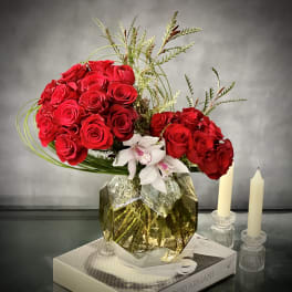 Red roses arranged in a gold geometric vase with white orchids