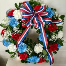 Round floral wreath with red, white, and blue carnations and a striped ribbon bow