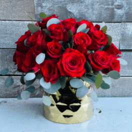 Red roses arranged in a gold vase with eucalyptus accents