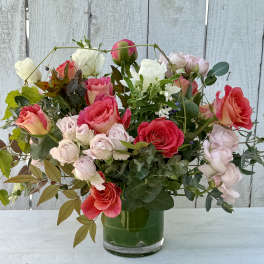 Mixed pink, coral, and white roses arranged in a glass vase