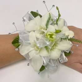 White orchid wrist corsage with silver ribbon and beaded accents on a hand