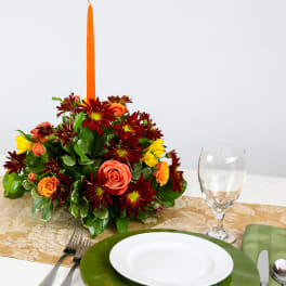 Autumn floral centerpiece with a tall orange candle on a table setting