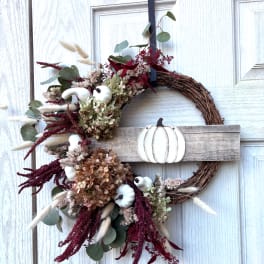 Fall wreath with dried flowers, eucalyptus, and white pumpkin accents on a wood door sign
