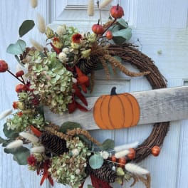 Fall wreath with dried flowers, pinecones, and a pumpkin sign on a white door