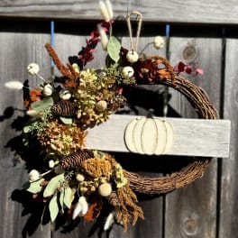 Fall wreath with dried flowers, pinecones, and a pumpkin sign on a wooden fence