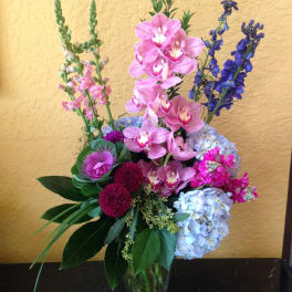 Tall bouquet of pink orchids and blue hydrangeas in a glass vase