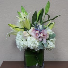White lilies and orchids arranged in a square glass vase
