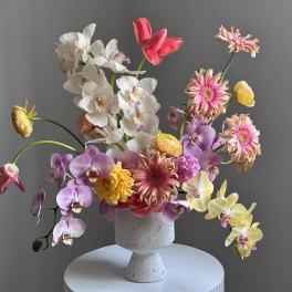 Mixed orchids and gerbera daisies in a white pedestal vase