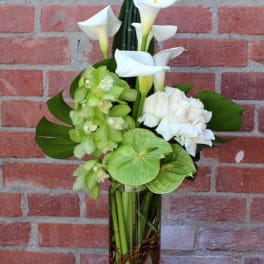 White calla lilies and green orchids in a tall glass vase