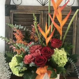 Tropical floral arrangement with red roses, hydrangeas, and orange bird-of-paradise in a white container
