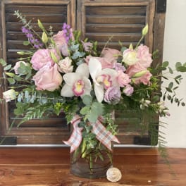 Pink and white floral arrangement in a glass vase with a plaid ribbon