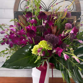 Tall magenta orchid arrangement in a white vase with a ribbon