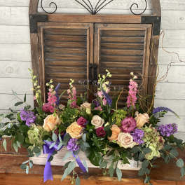 Low floral arrangement with roses, purple blooms, and greenery in a white container