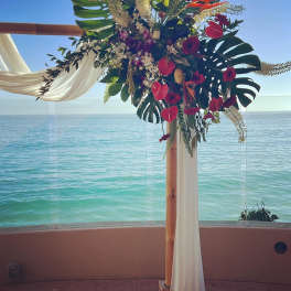 Tropical floral arch with red blooms and white draping by the ocean