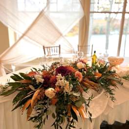 Low floral centerpiece with burgundy, peach, and cream blooms on a draped table
