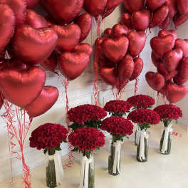 Red heart balloons above bouquets of red roses in glass vases