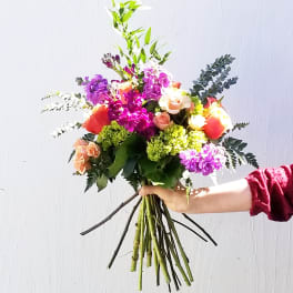 Handheld bouquet of mixed pink, purple, and peach flowers