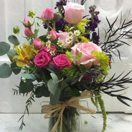 Mixed pink and purple bouquet in a glass vase with a raffia bow