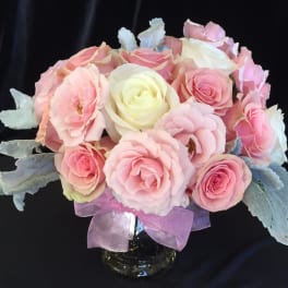 Pink and white rose bouquet in a glass vase with a purple ribbon