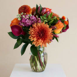 Colorful mixed bouquet in a clear glass vase with orange and purple blooms