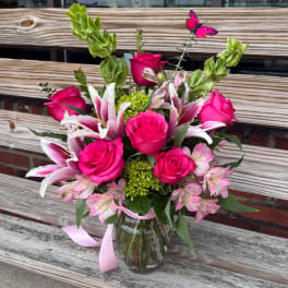Pink roses and lilies arranged in a glass vase with a ribbon.