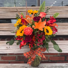 Bouquet of sunflowers, roses, lilies, and red blooms in a glass vase